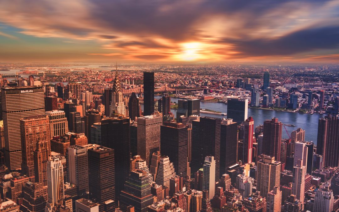 Aerial view of New York City skyline at sunset, highlighting iconic skyscrapers like the Chrysler Building and the MetLife Building, with the East River visible in the background.