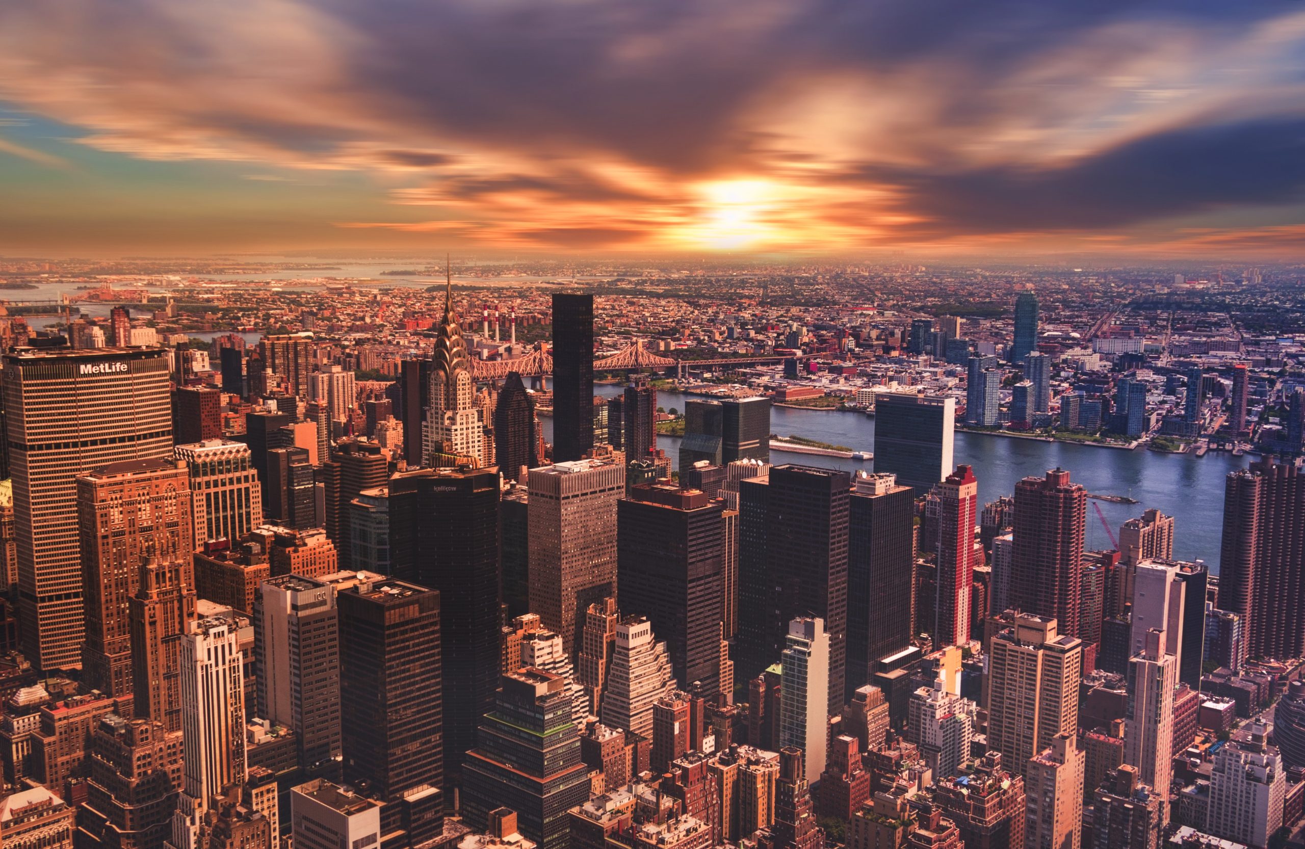 Aerial view of New York City skyline at sunset, featuring iconic skyscrapers like the Chrysler Building and MetLife, reflecting the urban landscape relevant to New York road test eligibility and driver&rsquo;s license information.