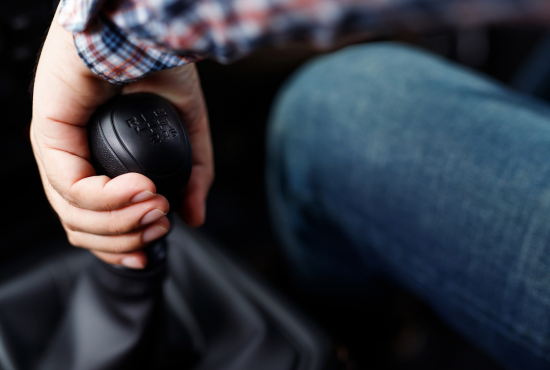 Hand gripping a manual transmission gear shift, demonstrating driving technique for road tests.