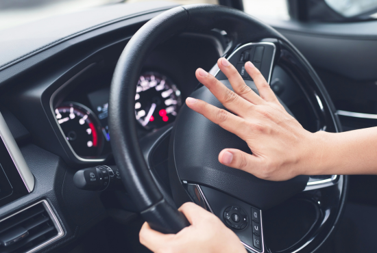 Driver's hand on steering wheel signaling with a honk, illustrating driving test scenarios and parallel parking challenges.