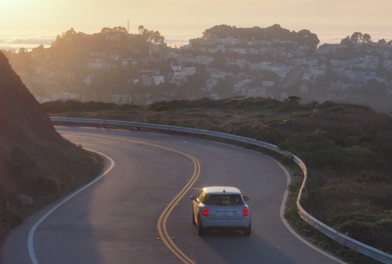 Car navigating a winding road at sunset, illustrating the challenges of driving on unfamiliar routes during a road test.