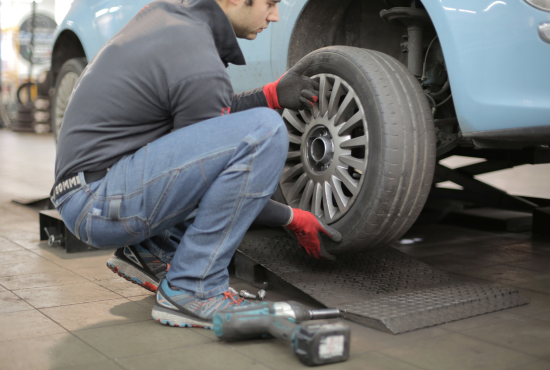 Mechanic using power tool to install a car tire in an automotive workshop, emphasizing tire maintenance and safety.