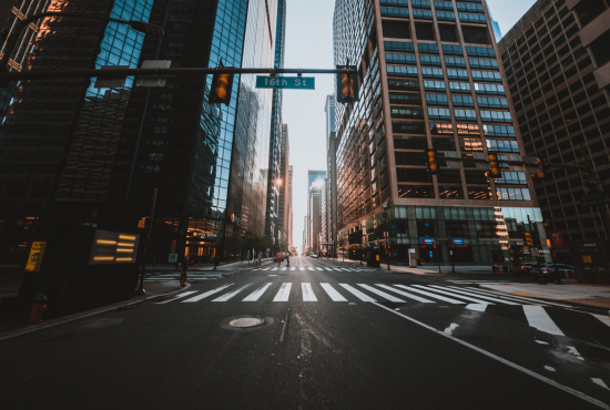 Empty urban street with crosswalks and skyscrapers, featuring a traffic signal at 16th Street, illustrating a city environment relevant to driving tests and road navigation.