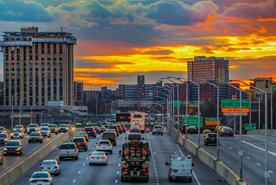 Traffic on a busy highway during sunset, with buildings in the background, illustrating urban driving conditions relevant to road test preparation.