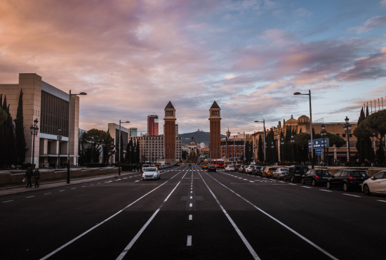 City street view featuring two iconic towers, surrounded by parked cars and buildings, under a colorful sunset sky, relevant for discussions on driving and road test experiences.