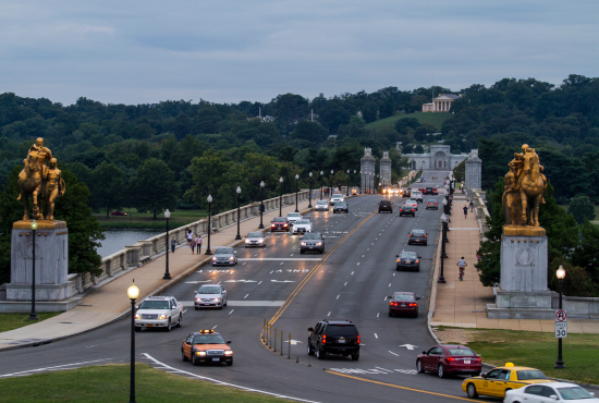 Bridge with vehicles and pedestrians, featuring golden lion statues at the entrance, set in a scenic park landscape, relevant to road test preparation and driving skills in New York.
