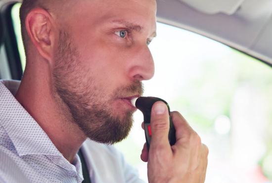 Man using a breathalyzer device in a car, emphasizing safety measures for road tests and driving compliance.