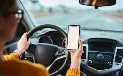 Person driving a car holding a smartphone, emphasizing road test preparation and safe driving practices in New York.